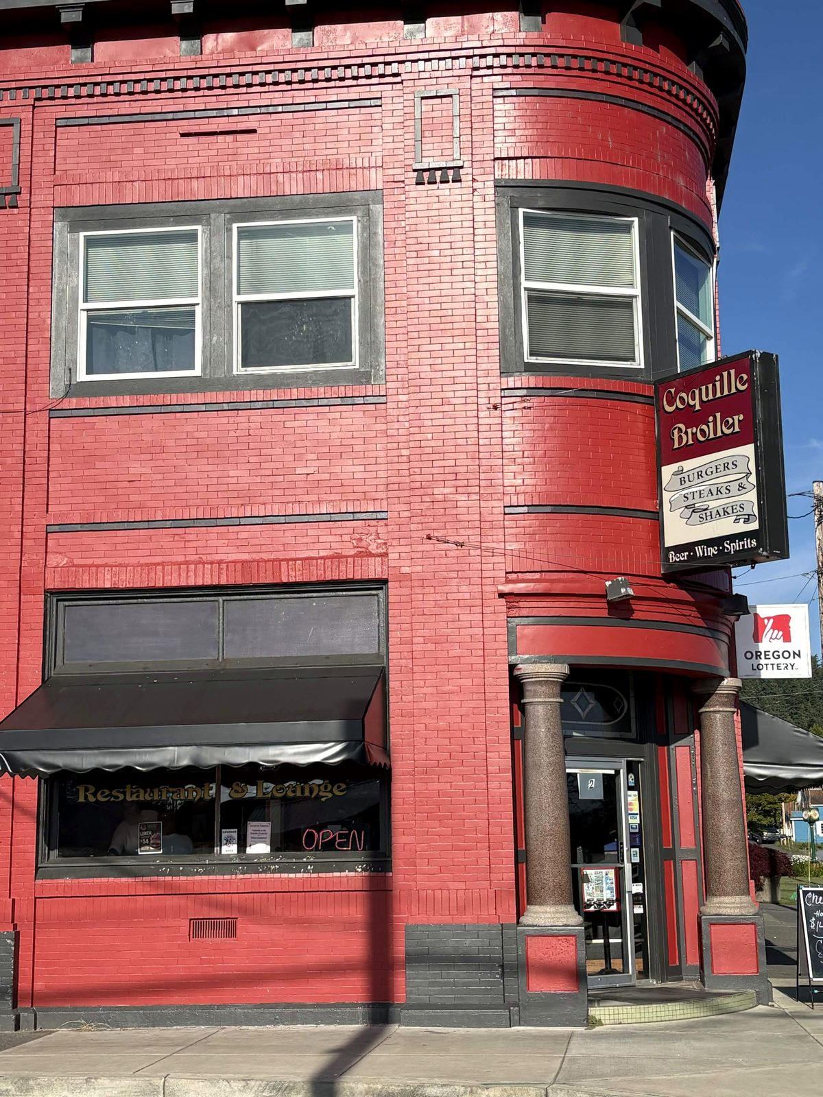 The Coquille Broiler entrance on the corner, with its columned doorway, hanging Burgers Steaks and Shakes sign, and Restaurant and Lounge lettering on the red brick building